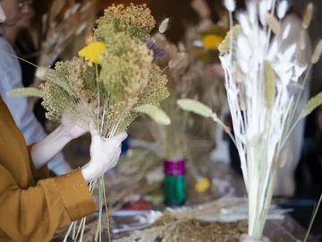 Hände halten Trockenblumensträuße in einem kreativen Workshop.