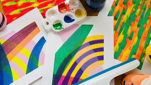 Colourful paintings on paper lie next to paint pots.