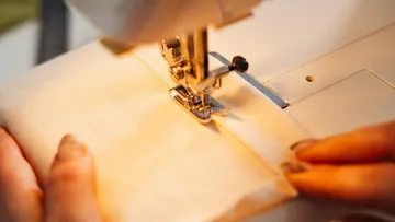 Sewing machine sews fabric, hands guide the material.