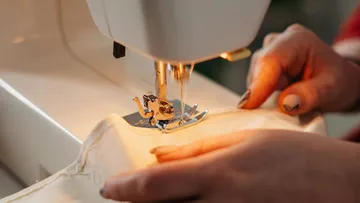 A sewing machine sews a fabric with human hands.