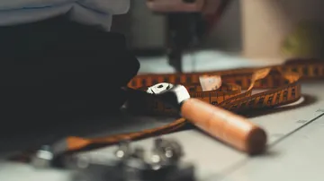Measuring tape and cutting tool on a tailor's table, blurred background with sewing machine, scene in a tailor's studio.