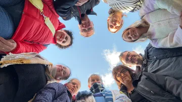 Gesichter von Menschen schauen nach unten, Himmel sichtbar.