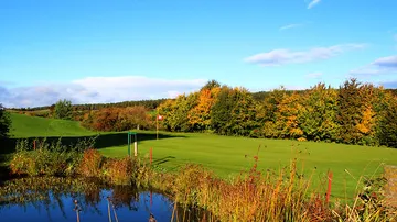 Green golf course with colorful trees and clear skies.