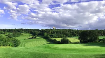 Golf course with green fairways, protected from trees and clouds.