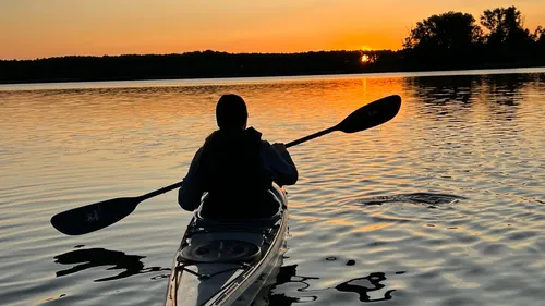 Kajakfahrer paddelt im Sonnenuntergang auf ruhigem Wasser.