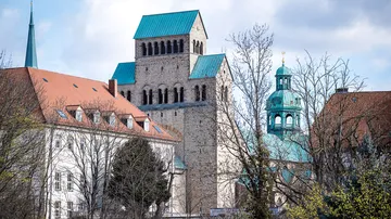 Houses and towers stand between trees and clouds.