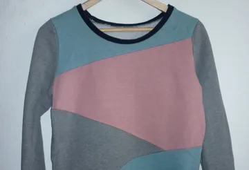 Colourful sweatshirt hangs on a wooden clothes hanger.