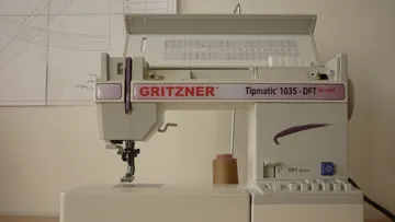 A sewing machine sews, stands on a table with a plan.