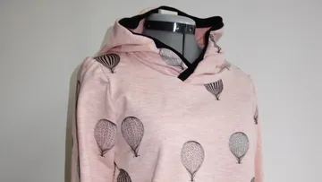 Pink sweater with balloons, slanted on a mannequin.