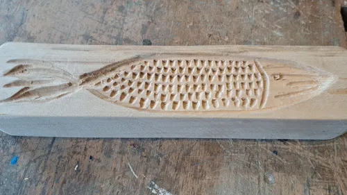 A wooden board with a fish pattern, carved on a workbench.