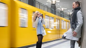 Eine Frau fotografiert einen Mann am Bahngleis.