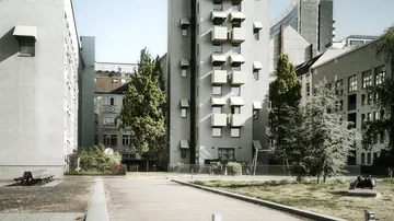 Graue Gebäude umgeben einen grünen Innenhof mit Bänken.