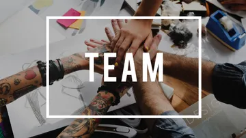 A team's hands are placed together on a table.