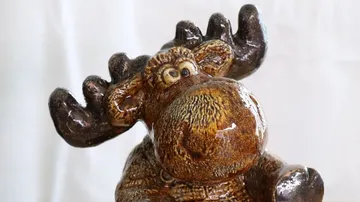 Glänzende Elchfigur steht mit aufgestellten Ohren vor Hintergrund.
