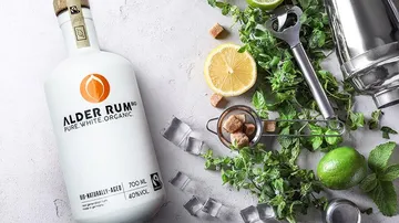 White rum stands next to lemons, limes and mint.