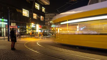 Yellow tram runs quickly through a busy city at night.