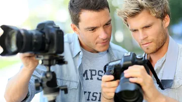 Two men look at a camera together on a tripod.