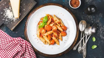 Pasta with tomatoes and basil served on a white plate.