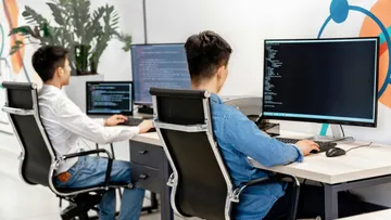 Zwei Personen programmieren an Computern in modernem Büro.