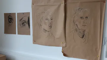 Three drawings of faces hang on the wall.