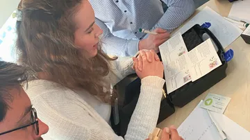 Drei Personen betrachten Unterlagen auf einem Tisch zusammen.