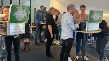 Personen stehen an hohen Tischen und interagieren mit Geräten.
