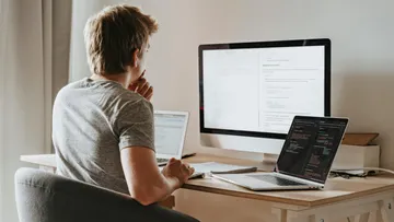 A person is sitting at a desk, working on a computer and laptop.