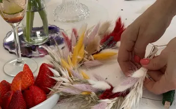 Hände binden einen bunten Trockenblumenkranz auf einem Tisch.