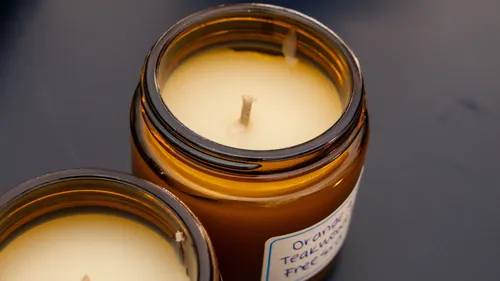 There are two candles on a table, one is burning.