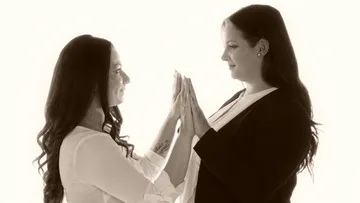 Two women touch each other with their hands, bright in the background.
