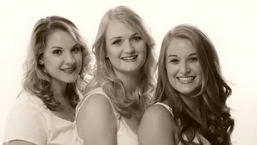 Three women smile pleasantly against a bright background.