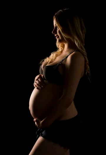Pregnant woman keeps her stomach in a dark room.