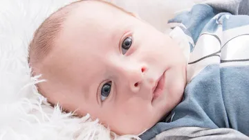 Baby lies on a soft white background and looks.