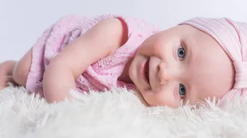 Baby liegt auf weichem Teppich und lächelt freundlich.