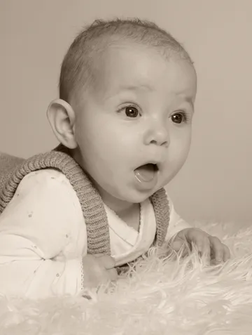 Baby's face shows surprise, lying on a soft background.