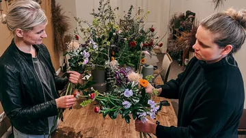 Zwei Frauen binden Blumensträuße am Tisch in einem Atelier.