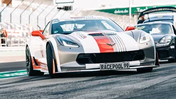 Sports car drives on racetrack, spectators in the background.