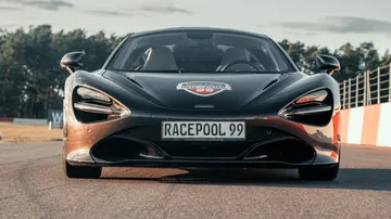 Black sports car drives on a racetrack with trees.