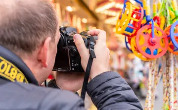 A photographer holds a camera in front of colorful toys.
