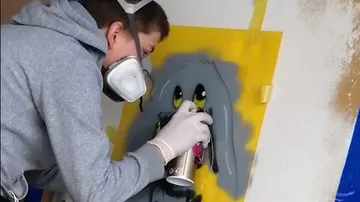 Boy sprays graffiti of a gray rabbit on the wall.
