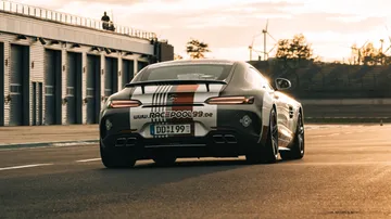 Sports car drives on a racetrack surrounded by buildings and trees.