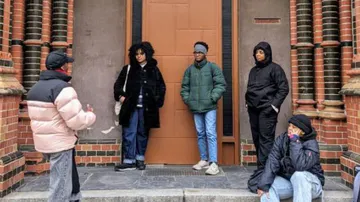 Six people stand in front of a door and talk.