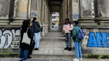 Six people stand under a row of graffiti-covered columns.