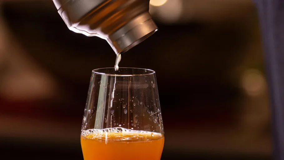 A cocktail is poured from a shaker into a glass.