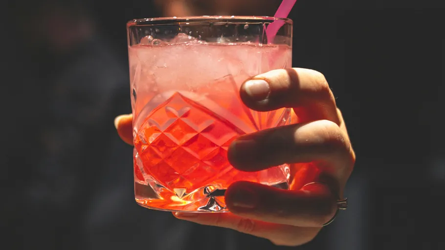 A glass of pink cocktail is held in the hand.