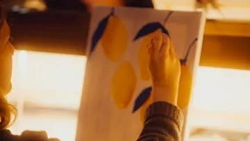 Person painting lemons on canvas indoors.