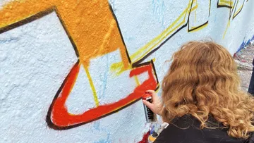 Eine Person sprüht roten Farbauftrag auf eine Wand.