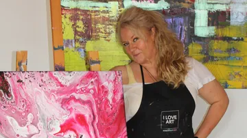 Künstlerin präsentiert rosa und weiße Malerei in Atelier.
