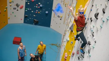 Climber moves on a wall, spectators watch her.