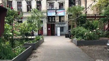Gartenweg, Pflanzen wachsen, Gebäude mit Restaurant im Hintergrund.